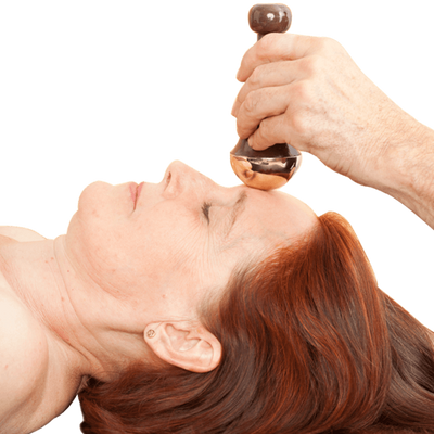 A person massaging a woman's face with Kansa Face and Body Wand